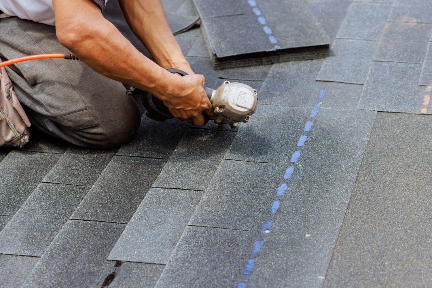 New asphalt bitumen shingles are being installed by roofer using pneumatic air nail gun