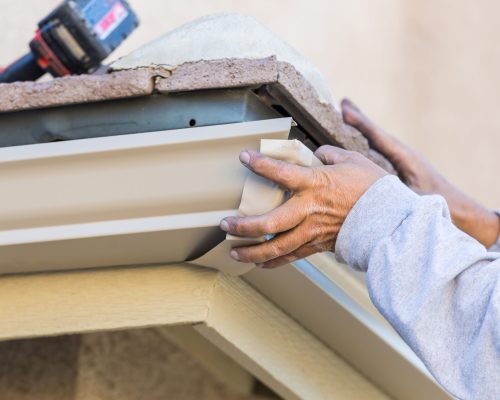 Worker Attaching Aluminum Rain Gutter to Fascia of House.